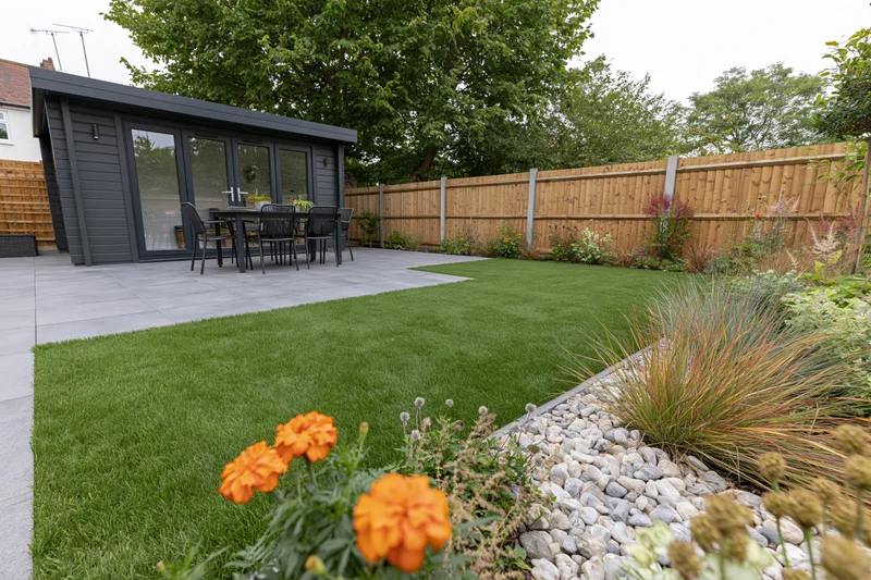 Freshly landscaped suburban backyard with artificial grass, patio, and garden shed surrounded by plants and wooden fence