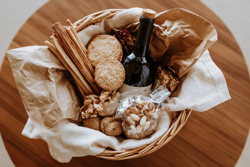 Overhead view of a gift basket filled with wine, crackers, breadsticks, nuts and cheese on a wooden table