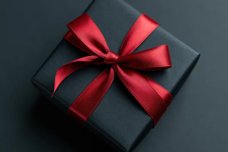 Black gift box wrapped in matte paper with red satin ribbon bow on dark surface