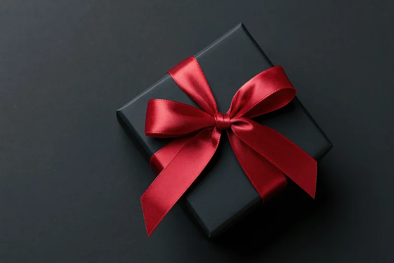 Black gift box with red satin ribbon bow on dark surface