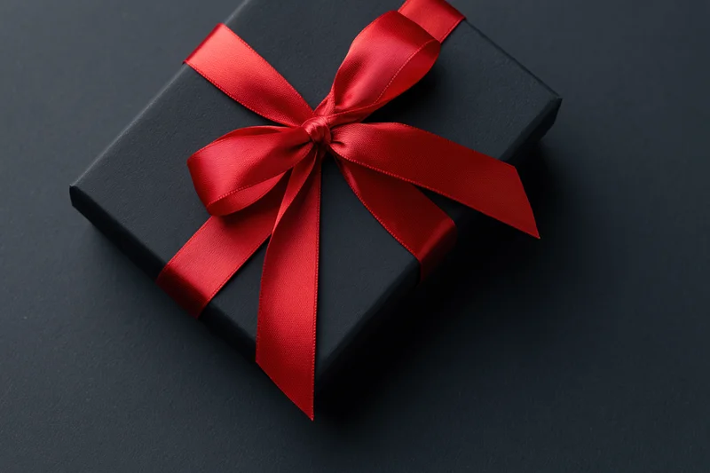 Black gift box with red satin ribbon bow on dark surface