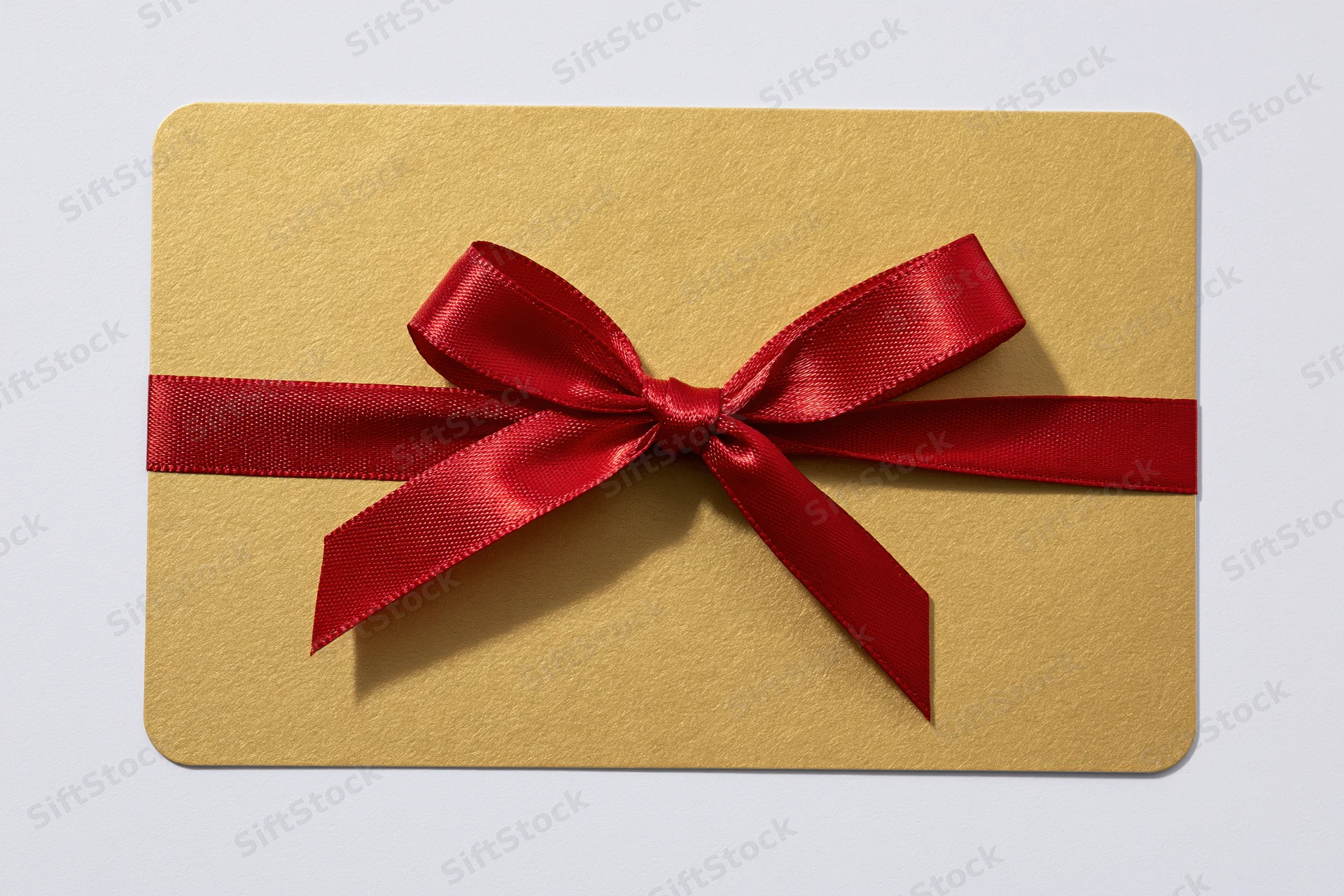 Gold gift card with red satin ribbon bow tied across center on white background