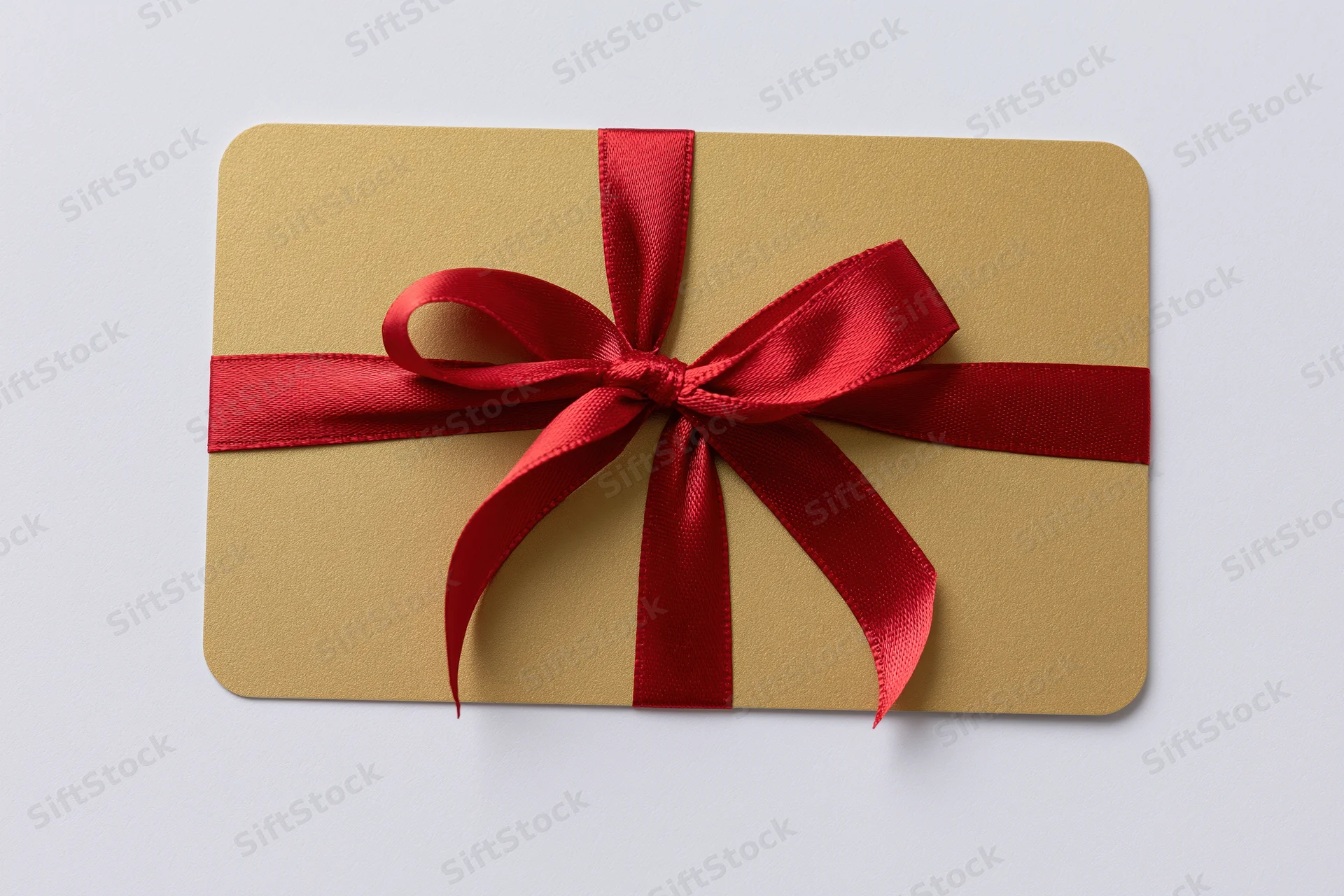 Gold gift card with red satin ribbon and bow tied across, isolated on white background