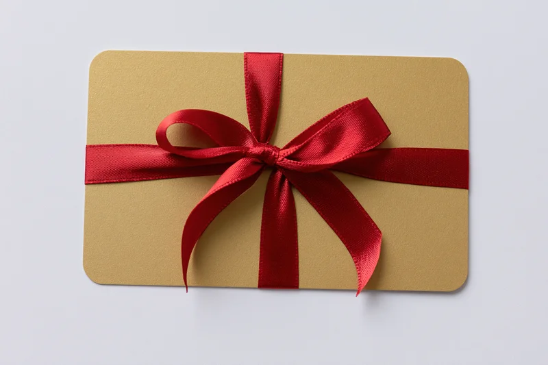 Gold gift card with red satin ribbon and bow tied across, isolated on white background