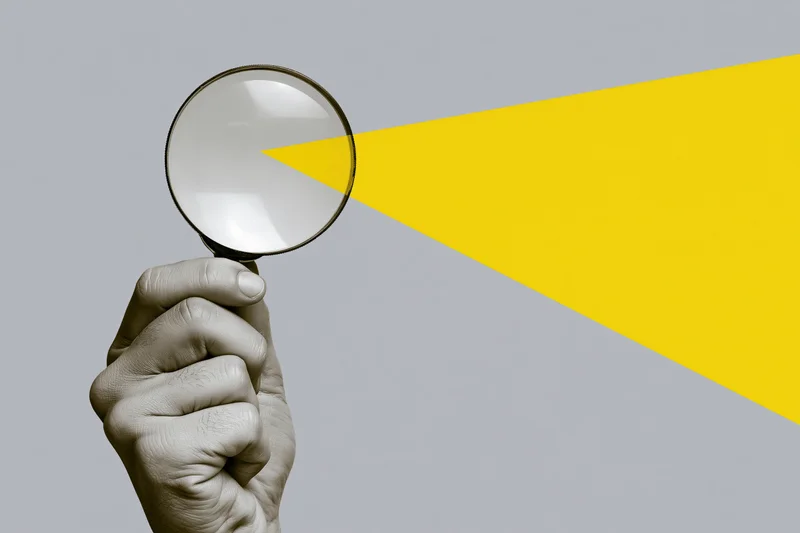 Hand holding magnifying glass against gray and yellow background