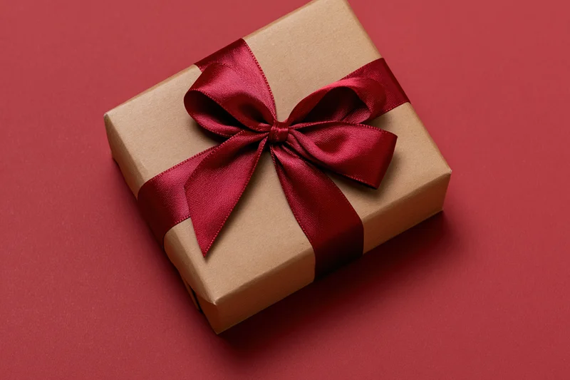 Kraft paper gift box tied with deep red satin ribbon on red background