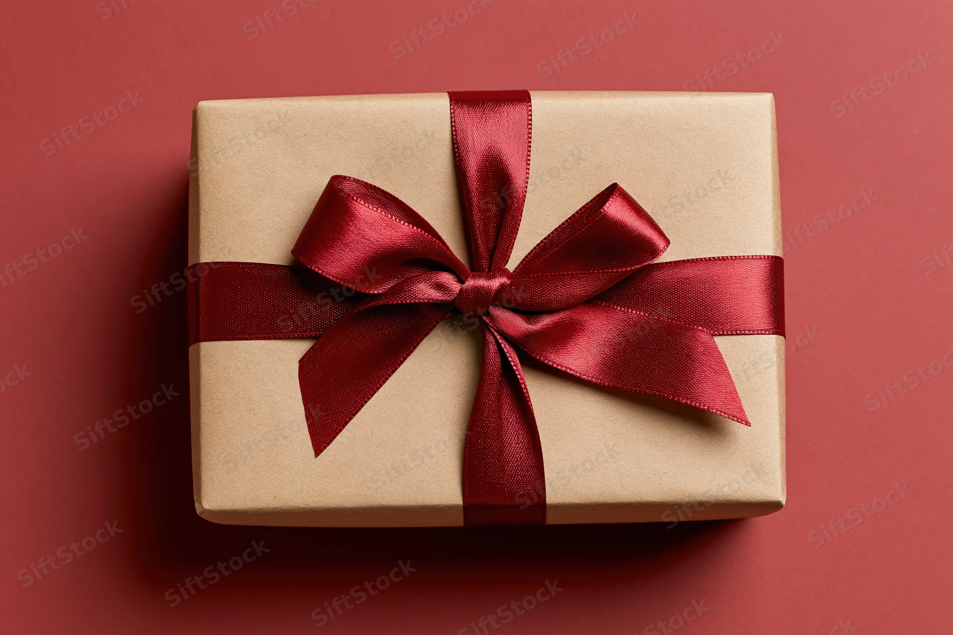 Gift box wrapped in kraft paper with red satin ribbon on red background