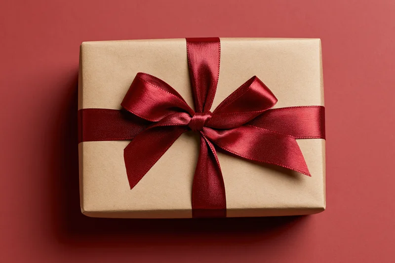 Gift box wrapped in kraft paper with red satin ribbon on red background