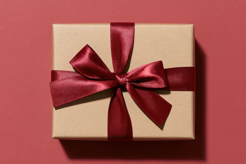Square kraft paper gift box with red satin ribbon bow on pink background