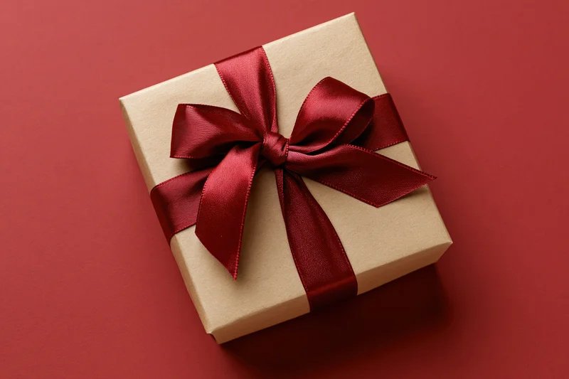 Kraft paper gift box tied with deep red satin ribbon on red background