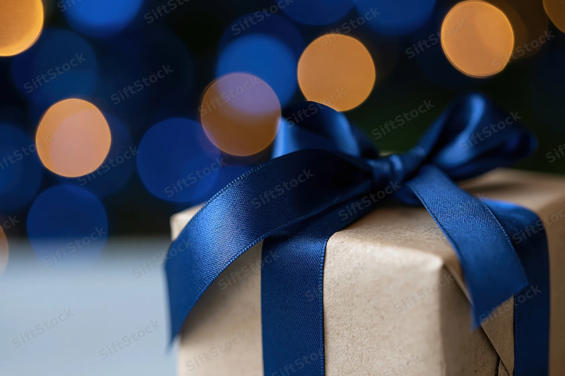 Kraft paper gift box tied with a glossy royal blue satin ribbon against blurred bokeh lights