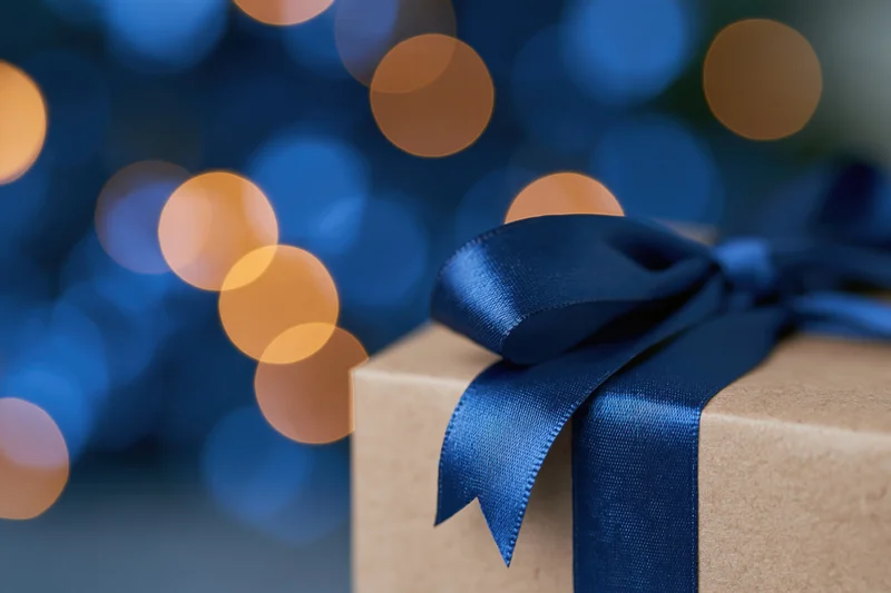 Kraft paper gift box with royal blue satin ribbon bow against blurred bokeh lights background