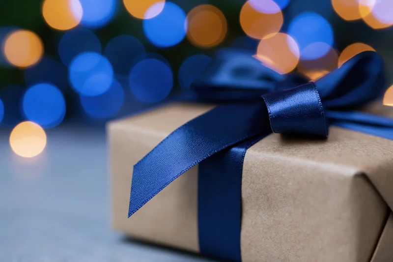 Gift box wrapped in kraft paper with blue satin ribbon against blurred holiday lights