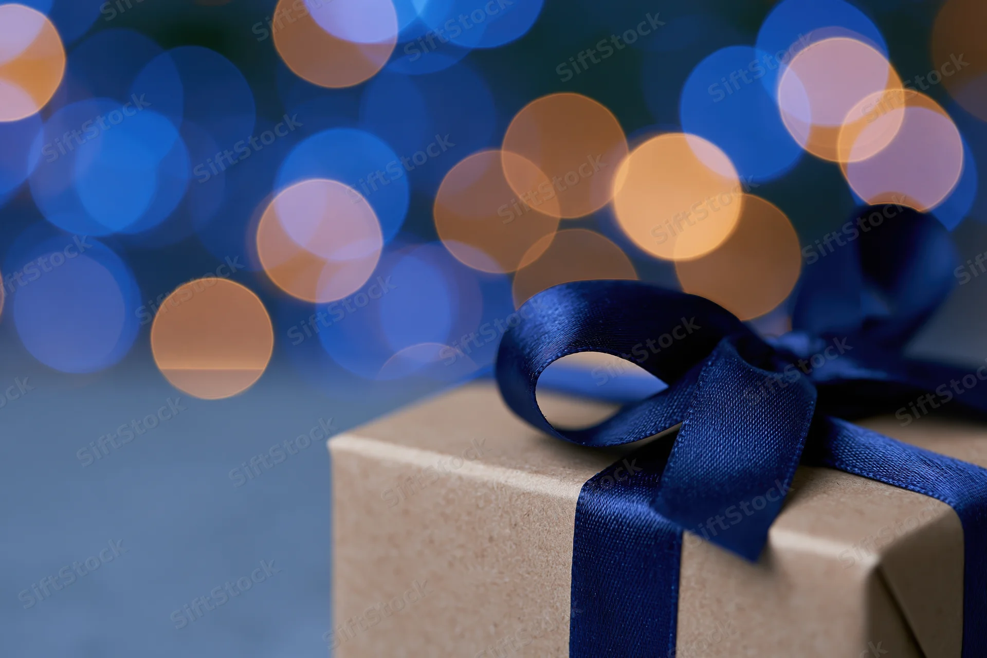 Kraft paper gift box with blue satin ribbon bow against blurred bokeh lights background
