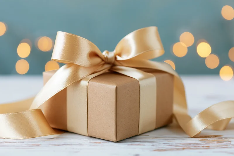 Kraft paper gift box tied with champagne satin ribbon on wooden surface with bokeh lights in background