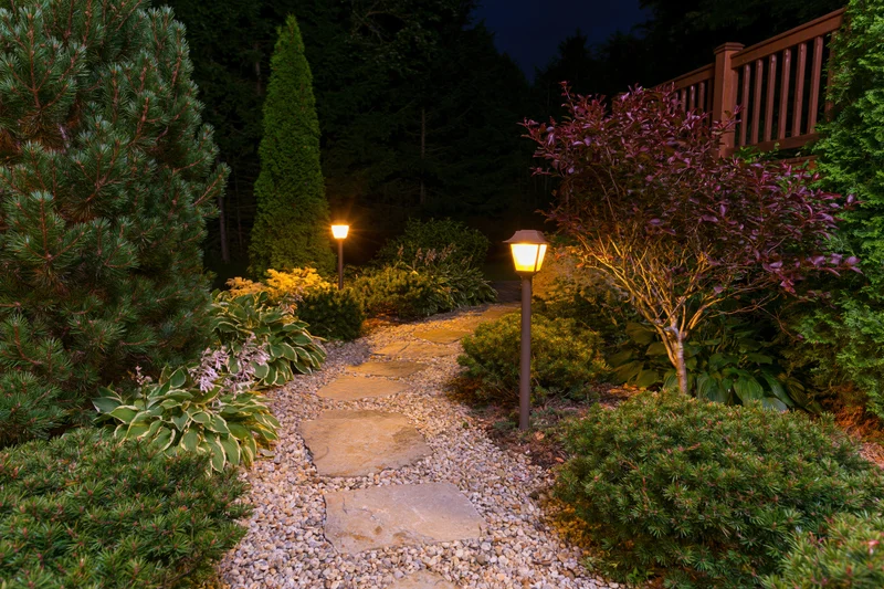Stone path through landscaped garden at night illuminated by bollard lamps