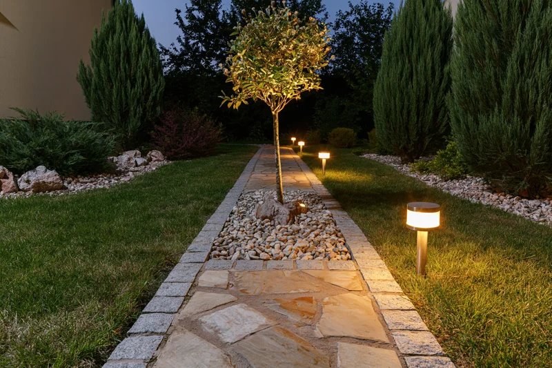 Stone pathway lined with bollard lights through a landscaped garden at night