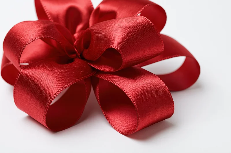 Large red satin gift bow with looped ribbon tails on white background