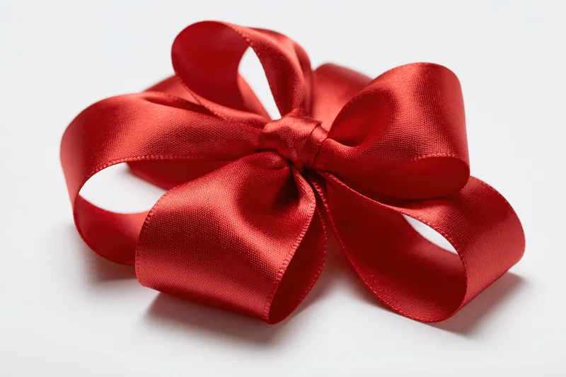 Large red satin gift bow with looped ribbon tails on white background