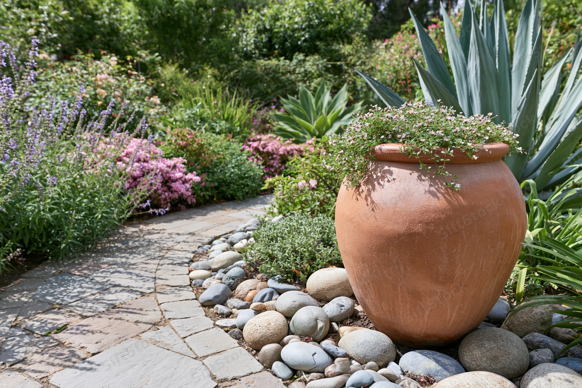 Large terracotta urn with trailing flowers beside a stone garden path surrounded by greenery and flowering plants