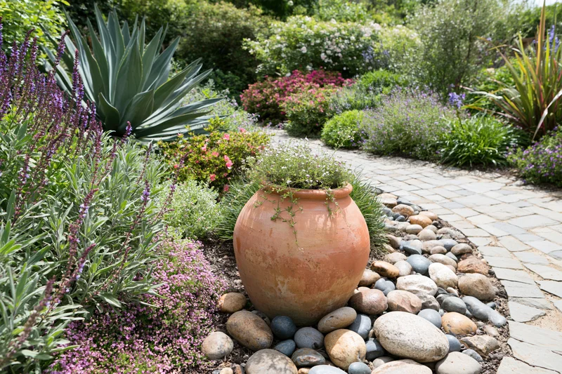 Large terracotta urn planted with flowers sits in garden