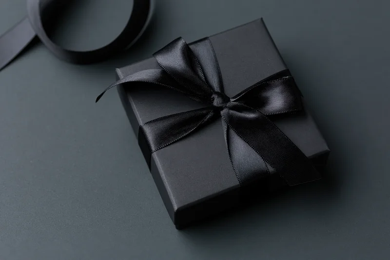 Matte black gift box tied with satin black ribbon bow on dark surface
