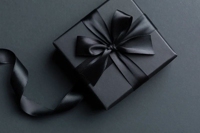 Matte black gift box tied with a satin black ribbon and bow on dark surface