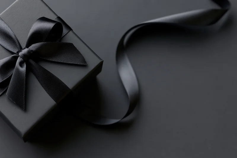 Matte black gift box with satin ribbon bow on dark surface