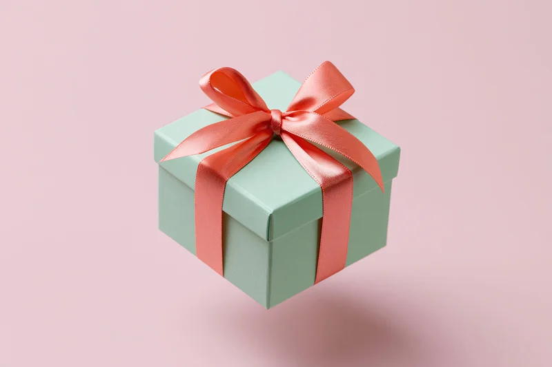 Mint-green gift box with coral-pink satin ribbon floating against a soft pink background