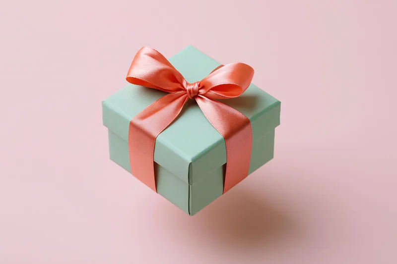 Mint-green gift box with coral-pink satin ribbon bow on pastel pink background