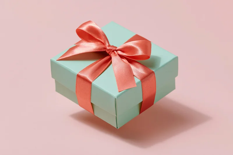 Mint-green gift box tied with coral-pink satin ribbon on soft pink background
