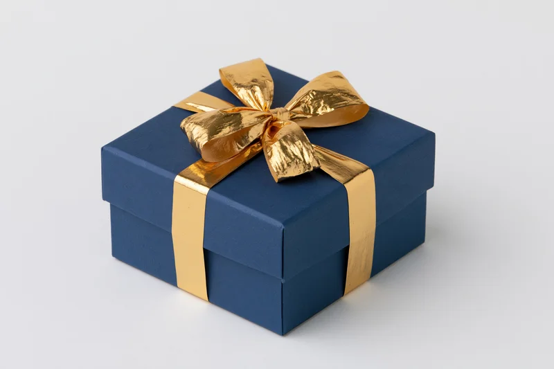 Navy blue gift box with gold metallic ribbon and bow on white background