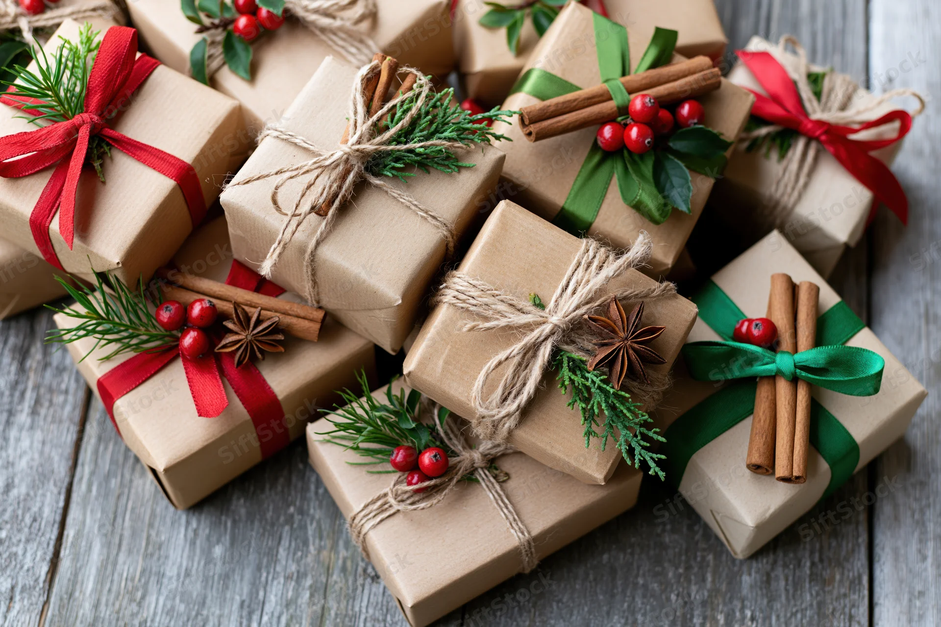 Kraft paper gift boxes wrapped with red and green ribbons and natural decorations on a wooden surface