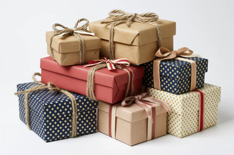 Stack of six wrapped gift boxes in various sizes and colors with ribbons and twine on white background