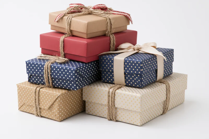 Stack of six wrapped gift boxes in various sizes and colors tied with twine and ribbon on white background