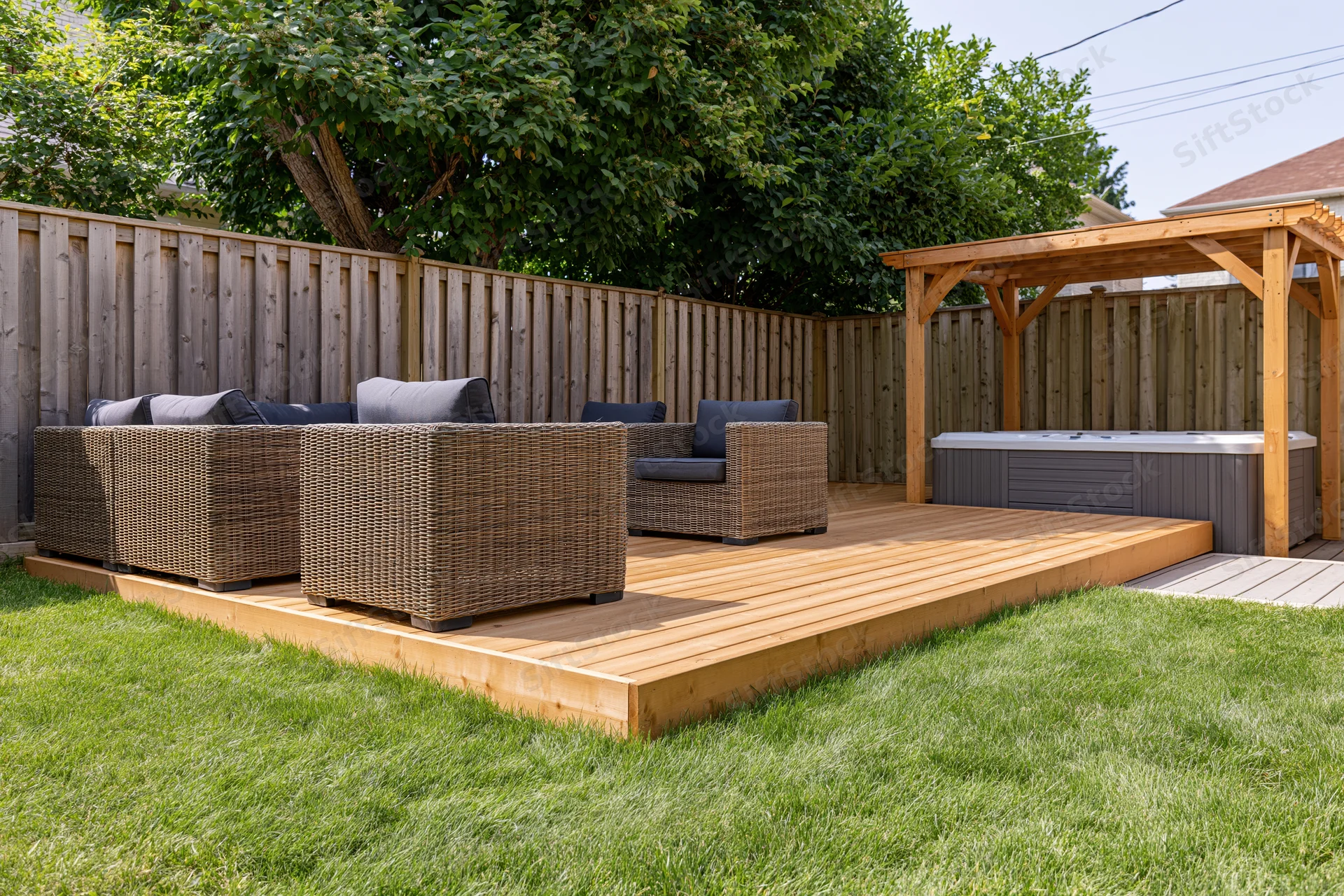 Wooden deck with wicker furniture and hot tub under pergola in private backyard garden