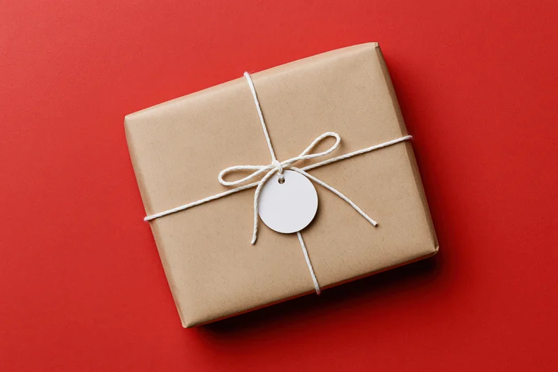 Rectangular gift box wrapped in brown kraft paper tied with white string and tag on red background