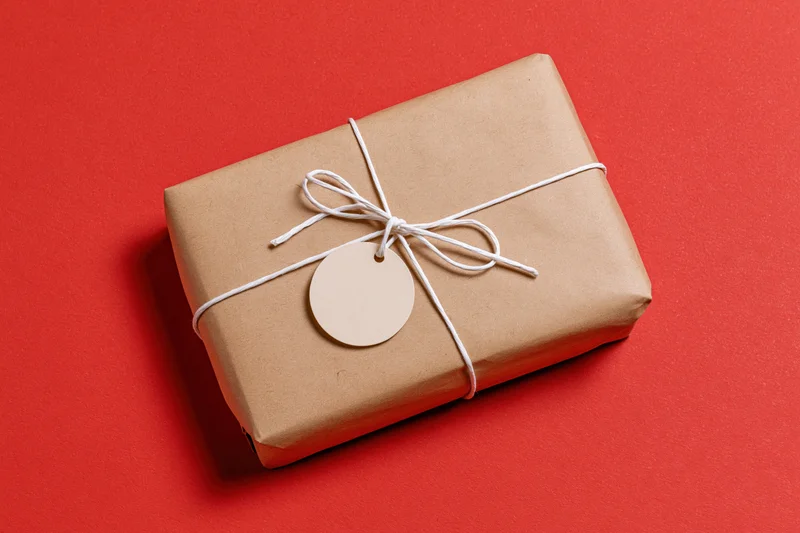 Rectangular gift box wrapped in brown kraft paper tied with white string and a blank circular tag on red background