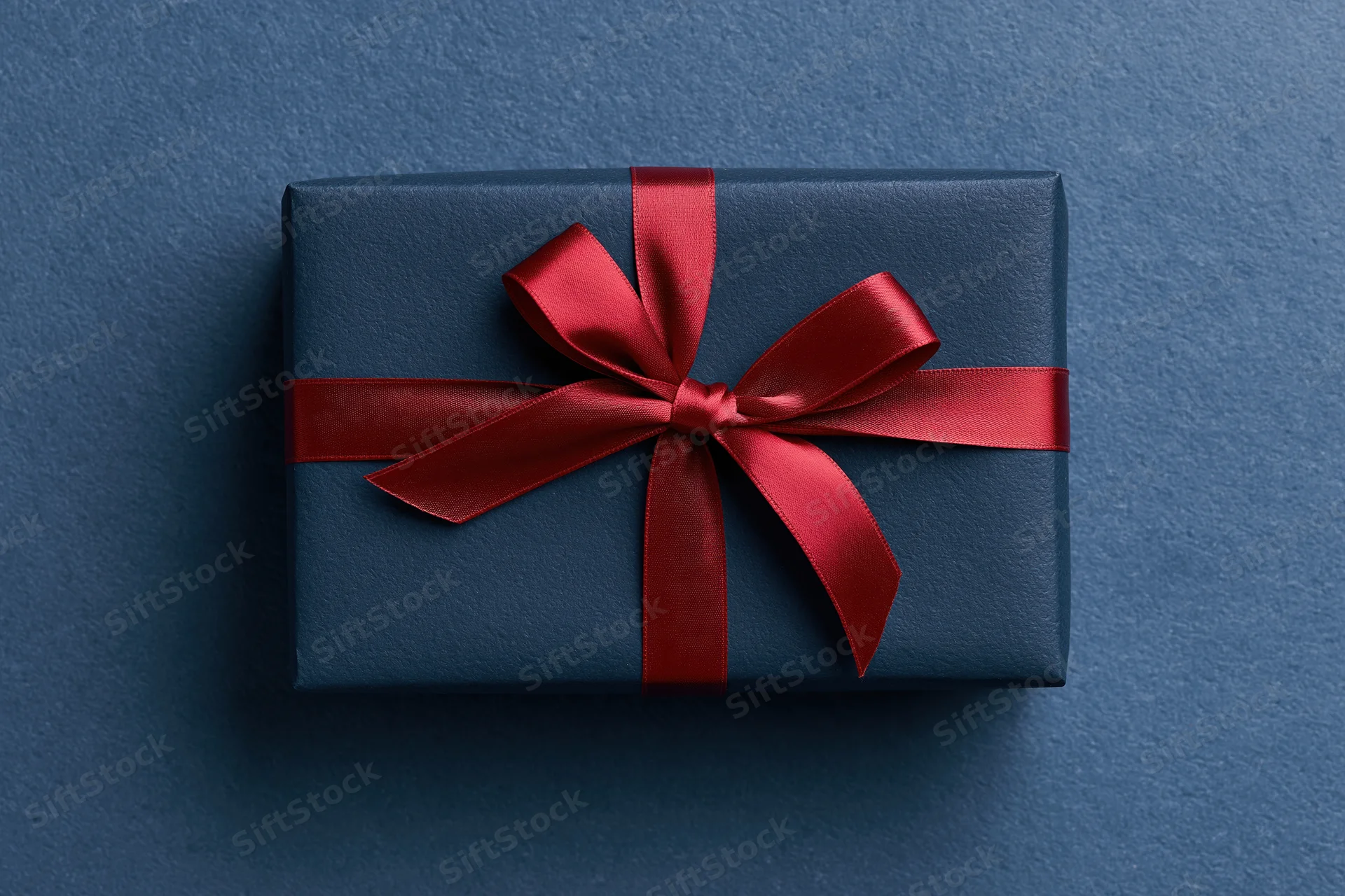 Navy gift box wrapped with red satin ribbon on blue textured surface