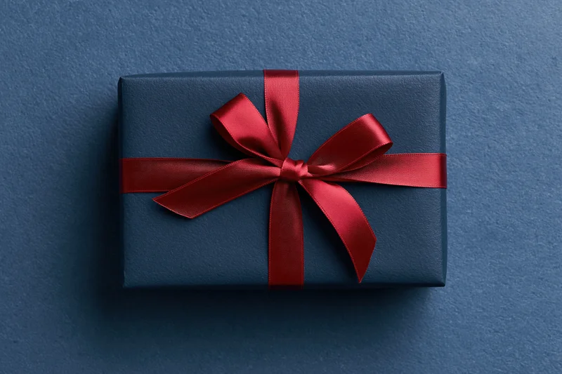 Navy gift box wrapped with red satin ribbon on blue textured surface