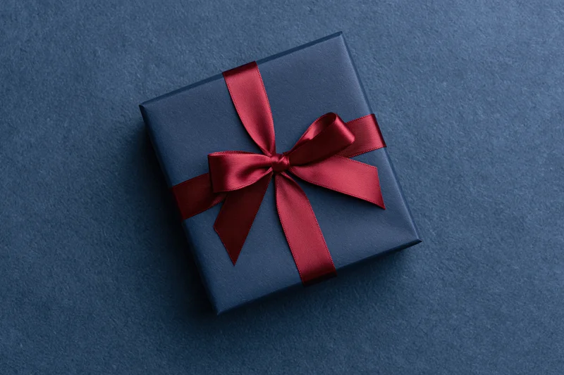 Navy gift box wrapped with red satin ribbon on textured blue surface