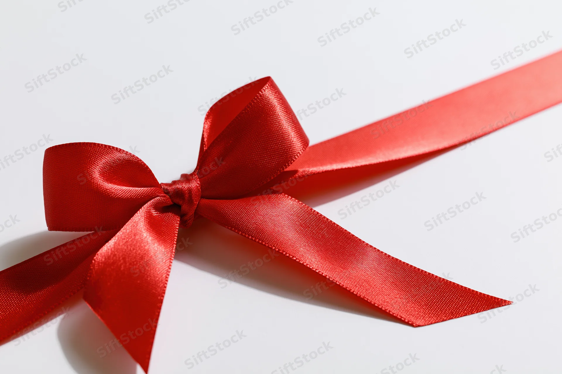 Red satin ribbon tied in a decorative bow on a white surface