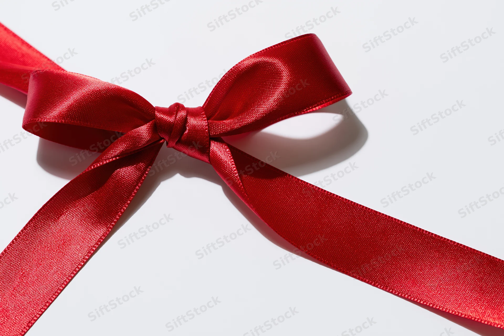 Red satin ribbon tied in a decorative bow on white background