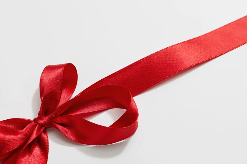 Red satin ribbon tied in a decorative bow on white background