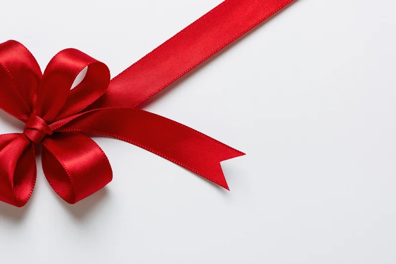 Red satin ribbon tied in a decorative bow on white background with copyspace