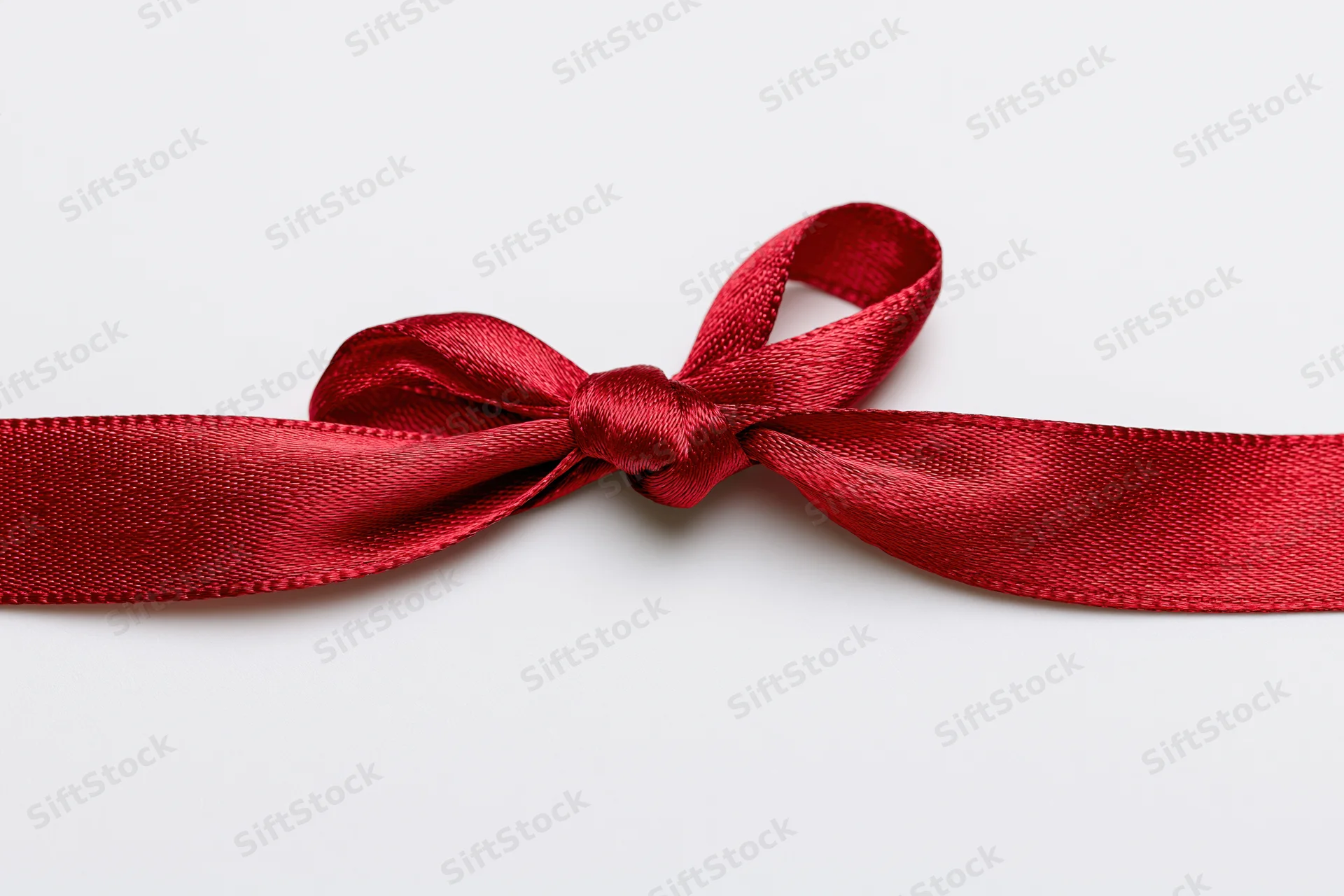 Red satin ribbon tied in a bow across a white background