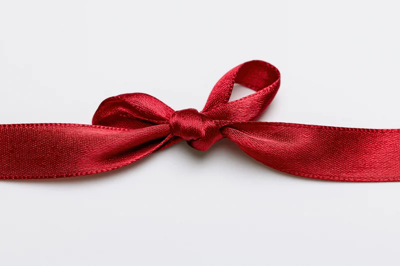 Red satin ribbon tied in a bow across a white background