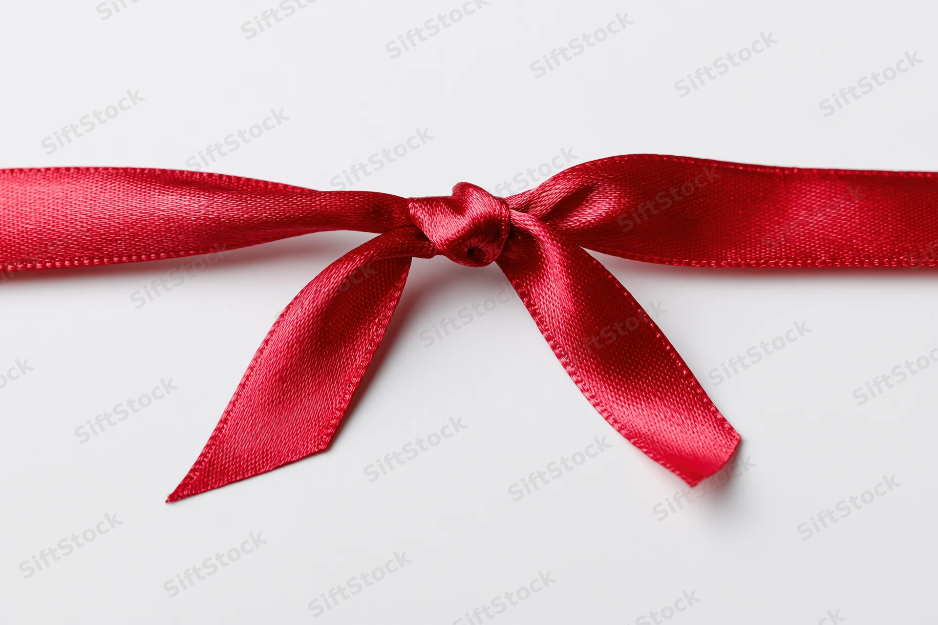 Red satin ribbon tied in a bow across a white surface