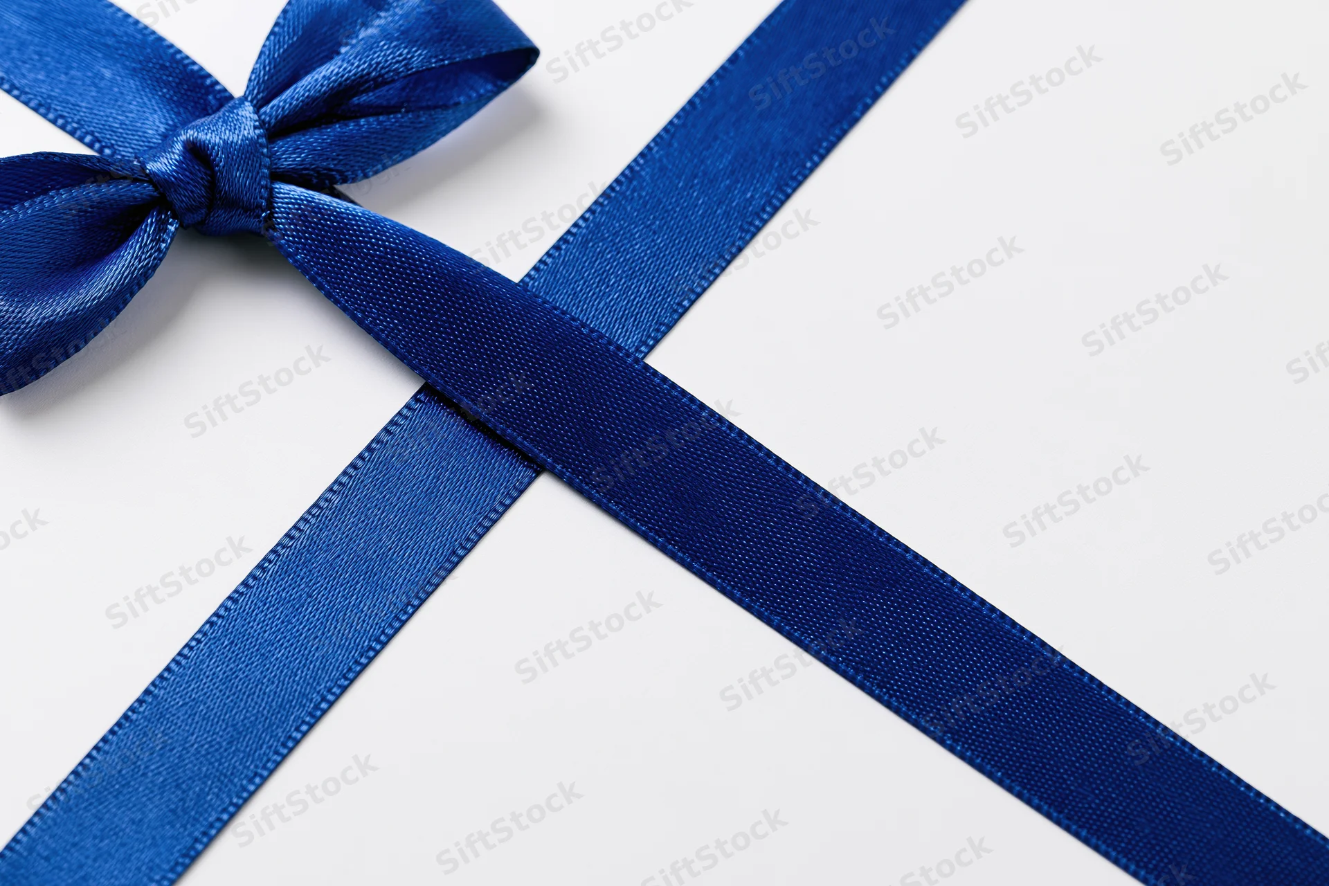 Royal blue satin ribbon tied in a bow with crossing tails on white background
