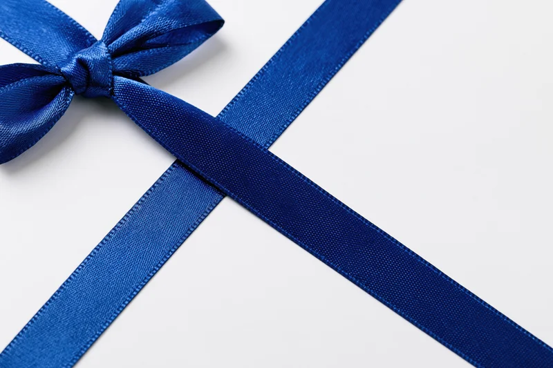 Royal blue satin ribbon tied in a bow with crossing tails on white background